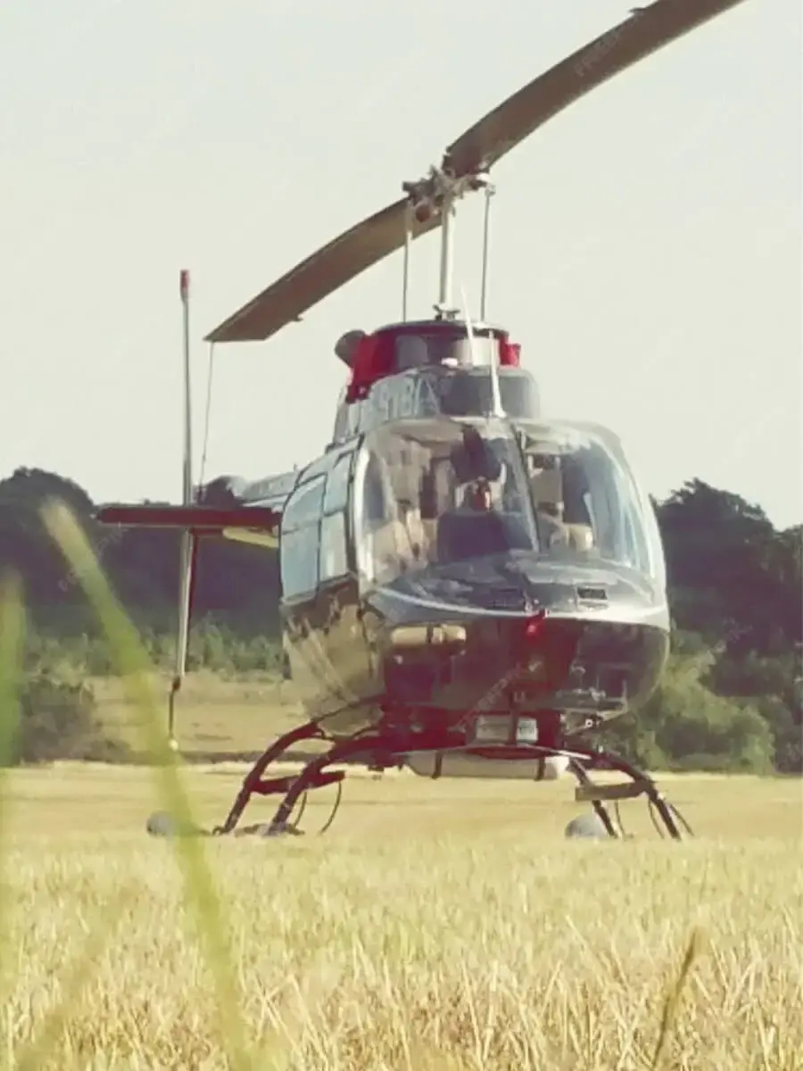 A safari helicopter waiting on a grass strip with its rotor turning